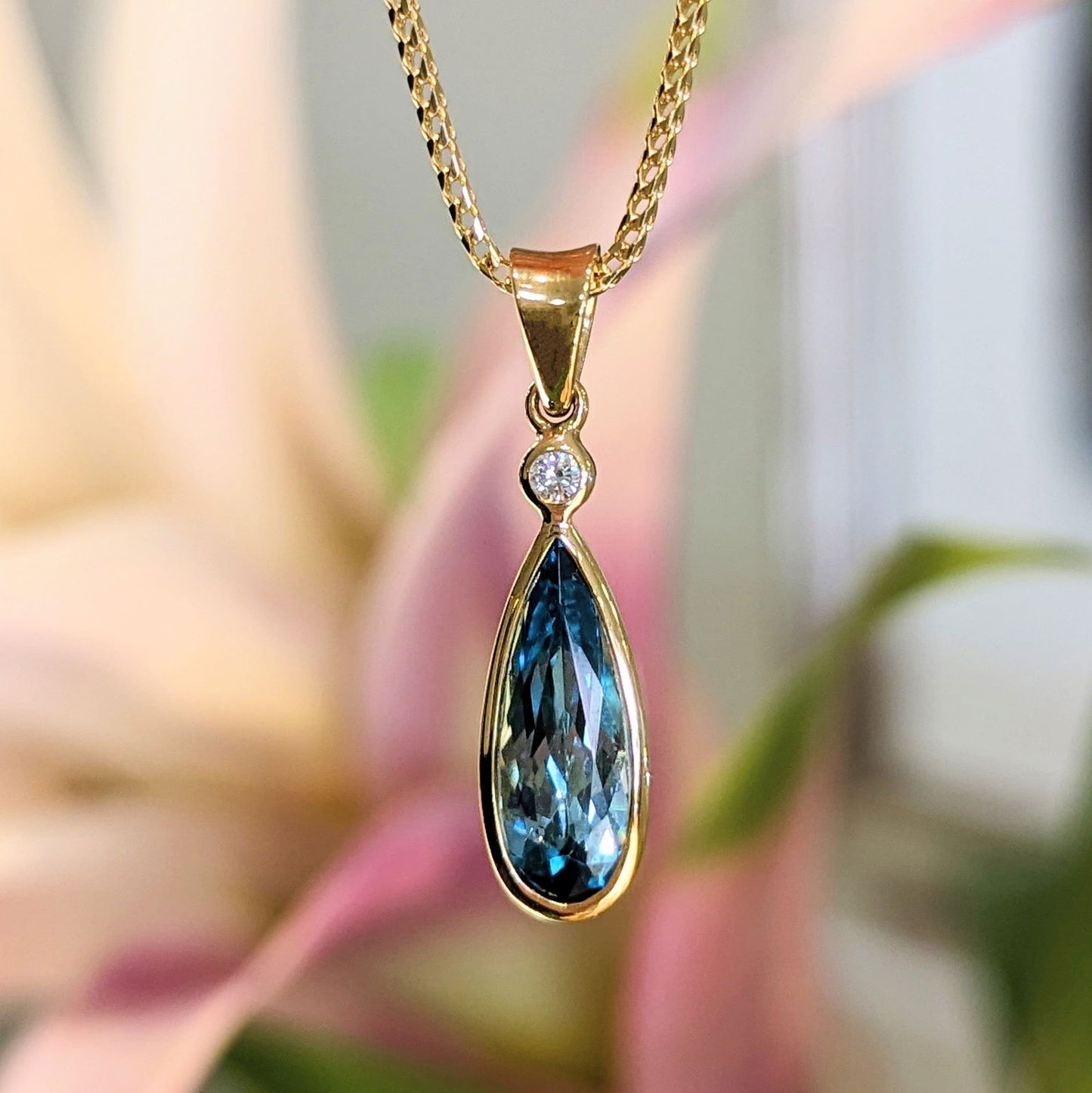 Photo of Blue-Green Zircon Teardrop Pendant in a decorative scene, designed by , available at Plumb Gold & Plumb Silver
