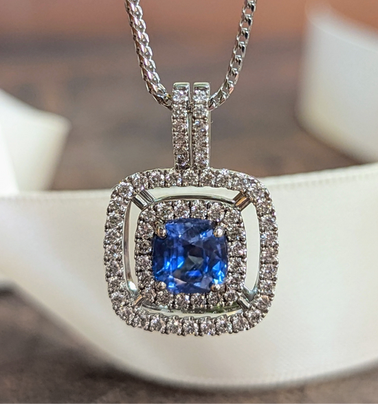 Photo of Blue Sapphire Cushion Double Halo Pendant in a decorative scene, designed by , available at Plumb Gold & Plumb Silver