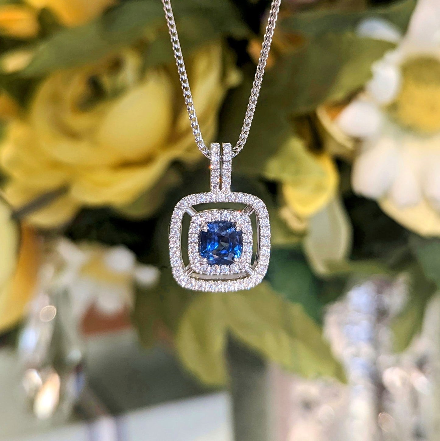Photo of Blue Sapphire Cushion Double Halo Pendant in a decorative scene, designed by , available at Plumb Gold & Plumb Silver