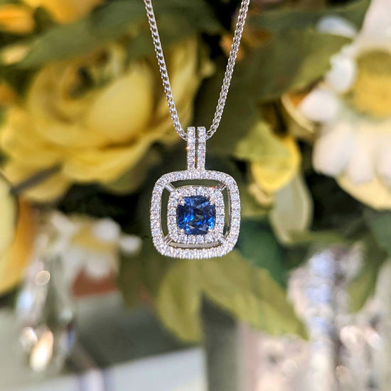 Photo of Blue Sapphire Cushion Double Halo Pendant in a decorative scene, designed by , available at Plumb Gold & Plumb Silver