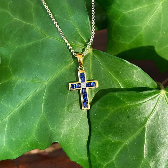 Photo of Blue Sapphire Diamond Cross Pendant in a decorative scene, designed by , available at Plumb Gold & Plumb Silver