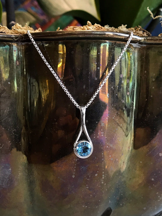Photo of Blue Topaz "Desire" Pendant in a decorative scene, designed by , available at Plumb Gold & Plumb Silver