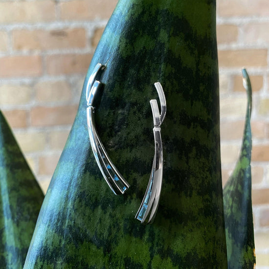 Photo of Blue Topaz Hinged Swoop Earrings in a decorative scene, designed by , available at Plumb Gold & Plumb Silver
