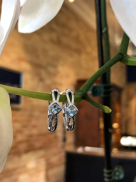 Photo of Blue Topaz Huggies in a decorative scene, designed by , available at Plumb Gold & Plumb Silver