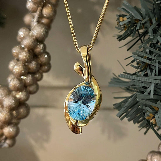 Photo of Blue Topaz Swoop Pendant in a decorative scene, designed by , available at Plumb Gold & Plumb Silver