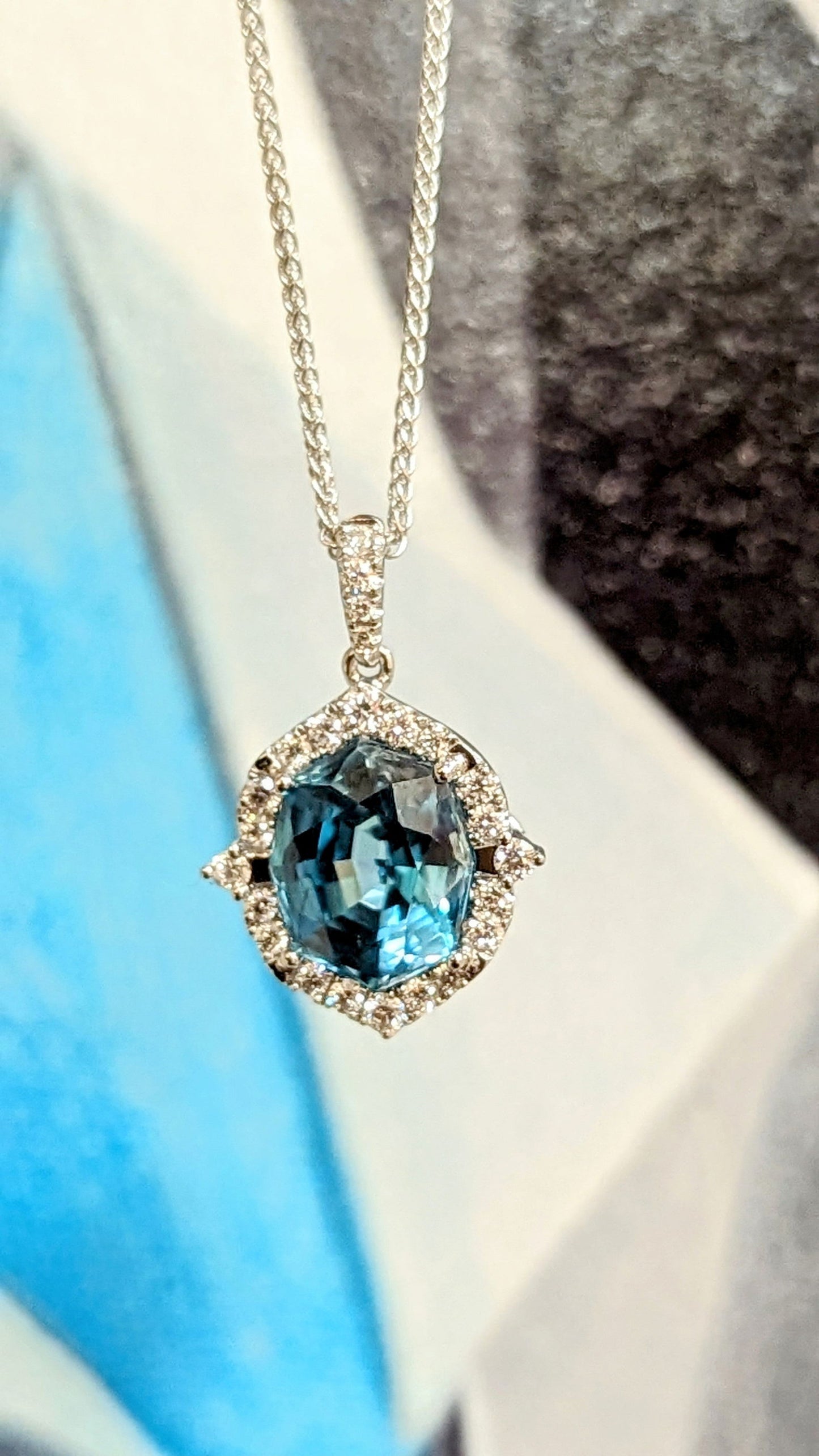 Photo of Blue Zircon Diamond Halo Pendant in a decorative scene, designed by , available at Plumb Gold & Plumb Silver