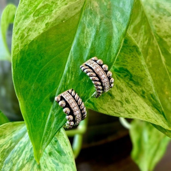 Photo of Braided Bangle Huggie Earrings in a decorative scene, designed by , available at Plumb Gold & Plumb Silver