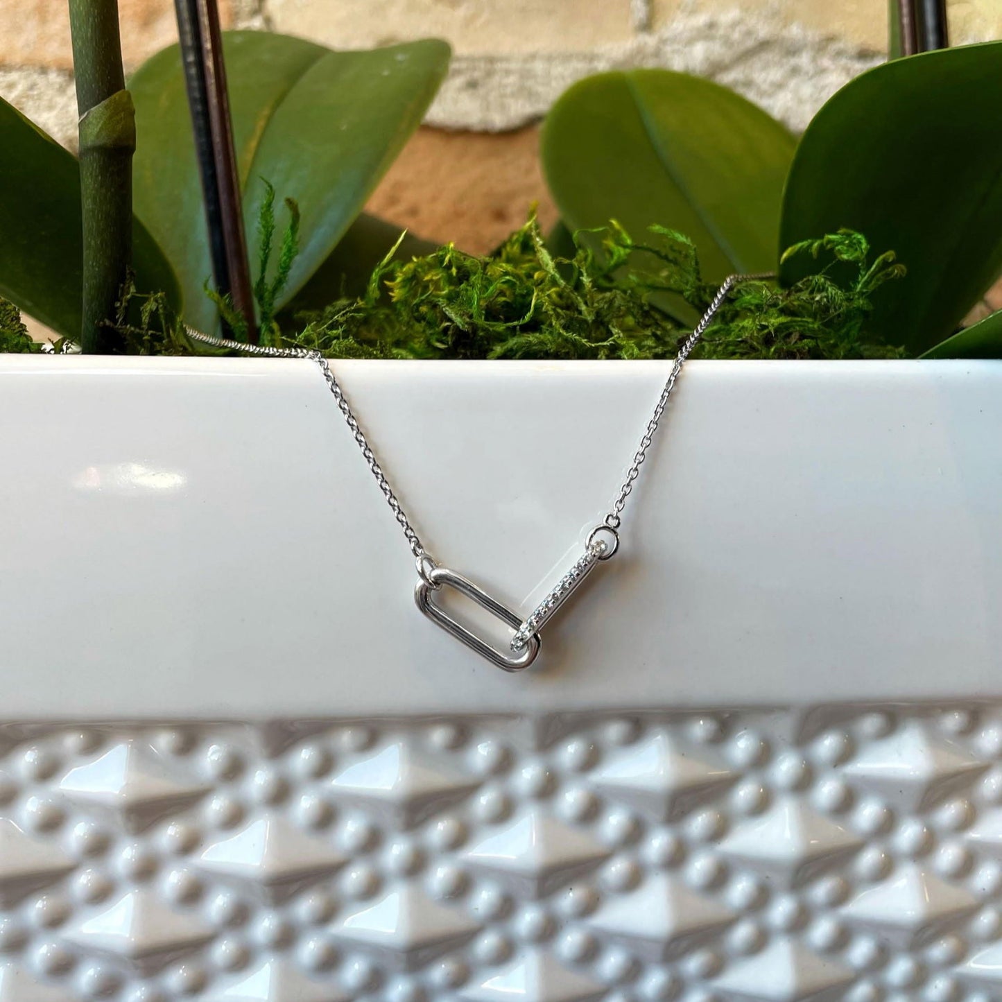 Photo of Cubic Zirconia Entwined Paperclip Necklace in a decorative scene, designed by , available at Plumb Gold & Plumb Silver