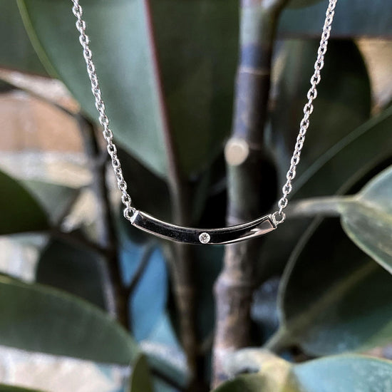 Photo of Curved Bar Necklace with Diamond Accent in a decorative scene, designed by , available at Plumb Gold & Plumb Silver