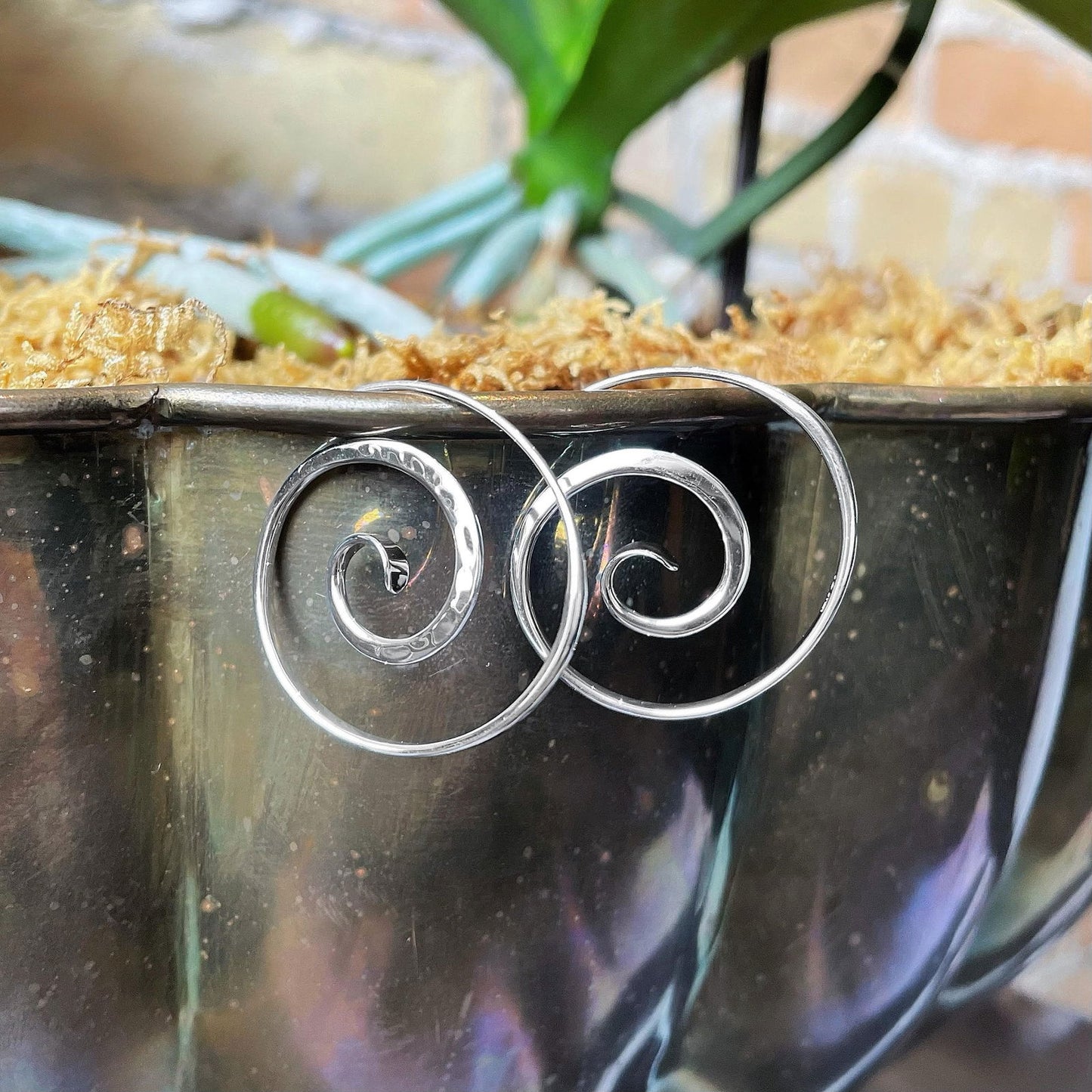 Photo of E L Designs "Crop Circle" Spiral Sterling Silver Hoop Earrings in a decorative scene, designed by , available at Plumb Gold & Plumb Silver