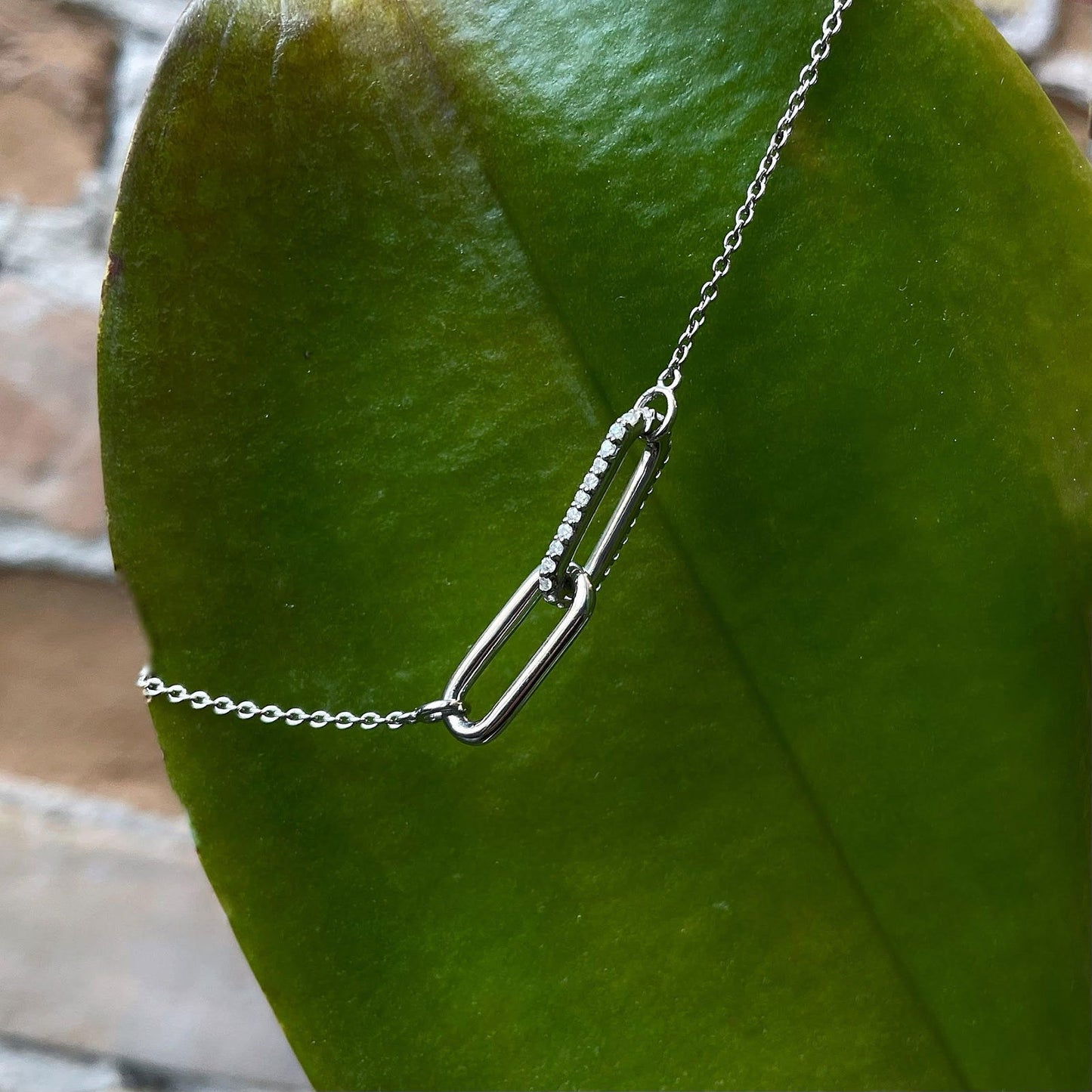 Photo of Entwined Cubic Zirconia Paperclip Bracelet in a decorative scene, designed by , available at Plumb Gold & Plumb Silver