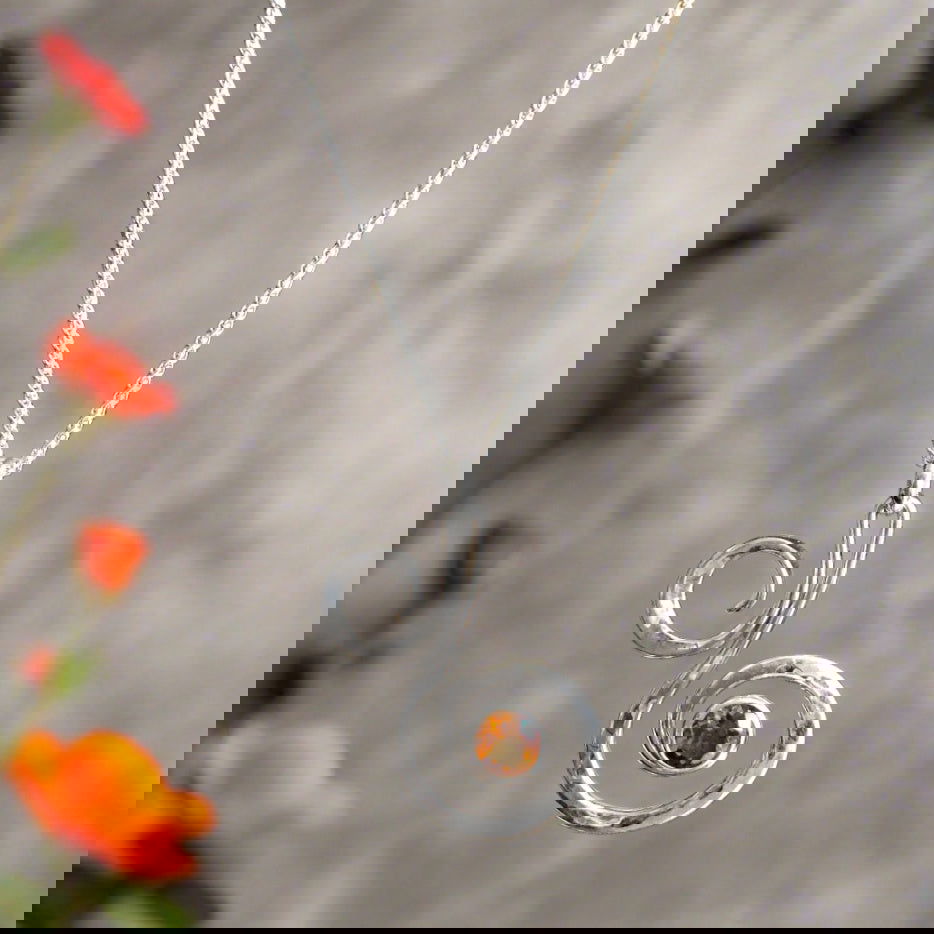 Photo of "Fiddlehead" Necklace in a decorative scene, designed by , available at Plumb Gold & Plumb Silver