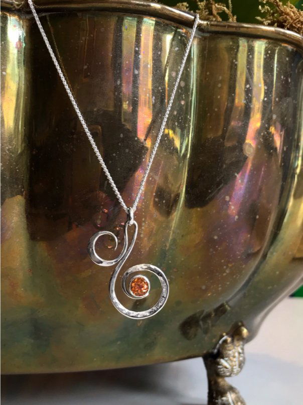 Photo of "Fiddlehead" Necklace in a decorative scene, designed by , available at Plumb Gold & Plumb Silver