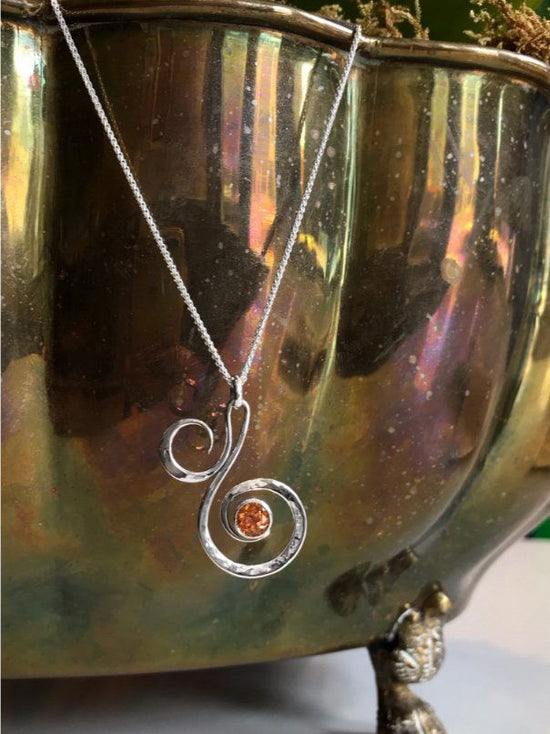 Photo of "Fiddlehead" Necklace in a decorative scene, designed by , available at Plumb Gold & Plumb Silver