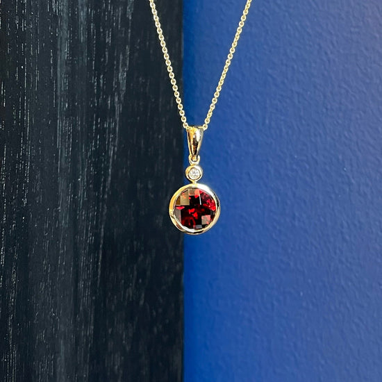 Photo of Garnet and Diamond Pendant in a decorative scene, designed by , available at Plumb Gold & Plumb Silver