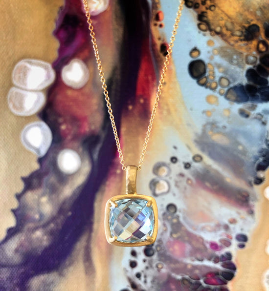 Photo of I. Reiss Blue Topaz Checkerboard Cut Gold Pendant in a decorative scene, designed by , available at Plumb Gold & Plumb Silver