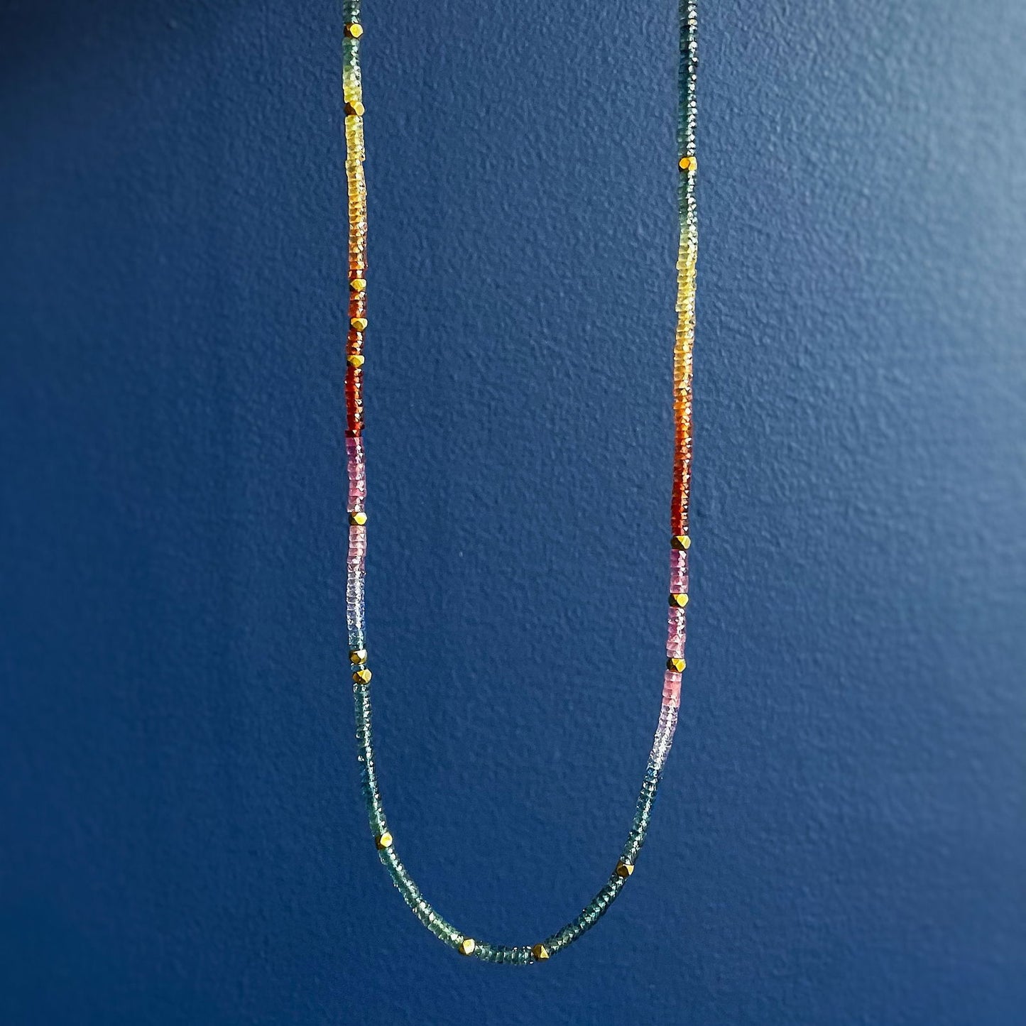 Photo of Kim Collins Rainbow Sapphire Necklace in a decorative scene, designed by , available at Plumb Gold & Plumb Silver