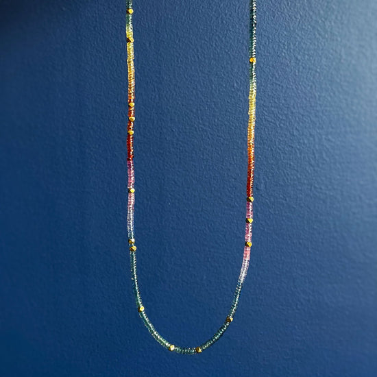 Photo of Kim Collins Rainbow Sapphire Necklace in a decorative scene, designed by , available at Plumb Gold & Plumb Silver