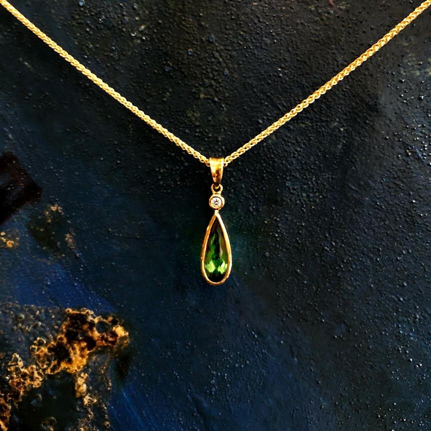 Photo of Pear-Shaped Green Tourmaline and Diamond Pendant in a decorative scene, designed by , available at Plumb Gold & Plumb Silver
