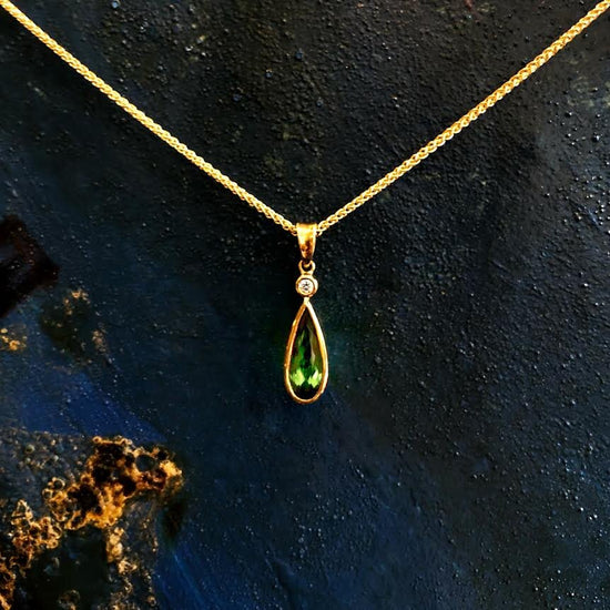Photo of Pear-Shaped Green Tourmaline and Diamond Pendant in a decorative scene, designed by , available at Plumb Gold & Plumb Silver