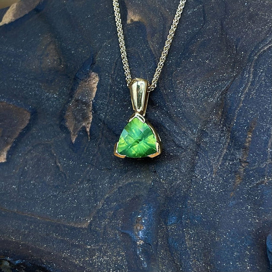 Photo of Peridot Trillion Pendant in a decorative scene, designed by , available at Plumb Gold & Plumb Silver