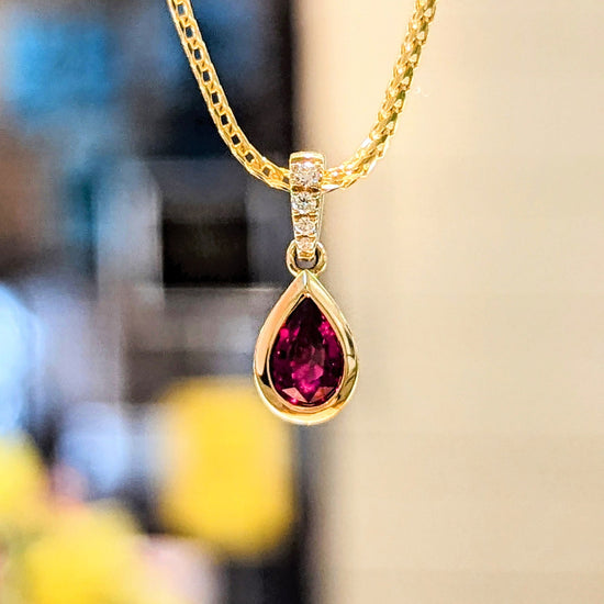 Photo of Petite Ruby and Diamond Pendant in a decorative scene, designed by , available at Plumb Gold & Plumb Silver
