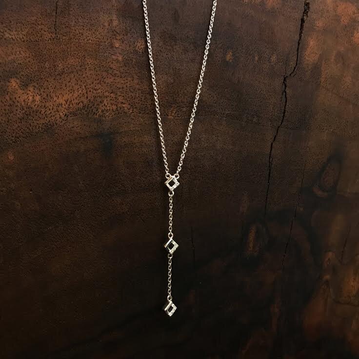 Photo of Petite Three Square Necklace in a decorative scene, designed by , available at Plumb Gold & Plumb Silver