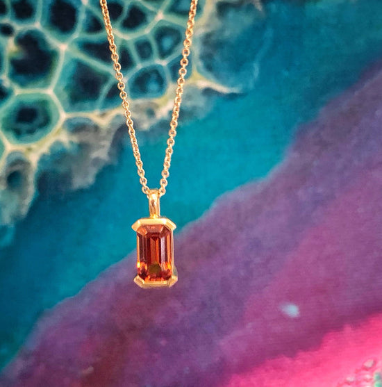 Photo of Spessartite Garnet Emerald Cut Gold Pendant in a decorative scene, designed by , available at Plumb Gold & Plumb Silver