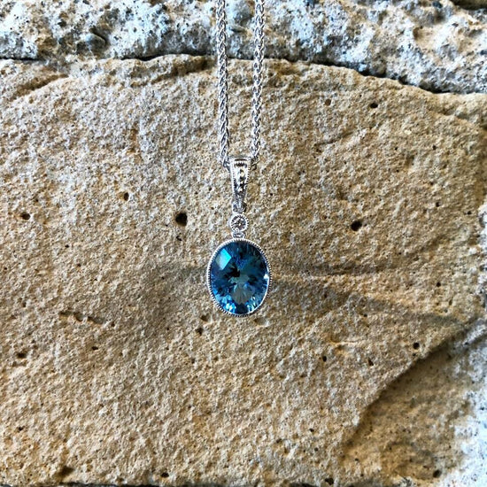 Photo of Stanton Color Oval Blue Topaz Pendant in a decorative scene, designed by , available at Plumb Gold & Plumb Silver
