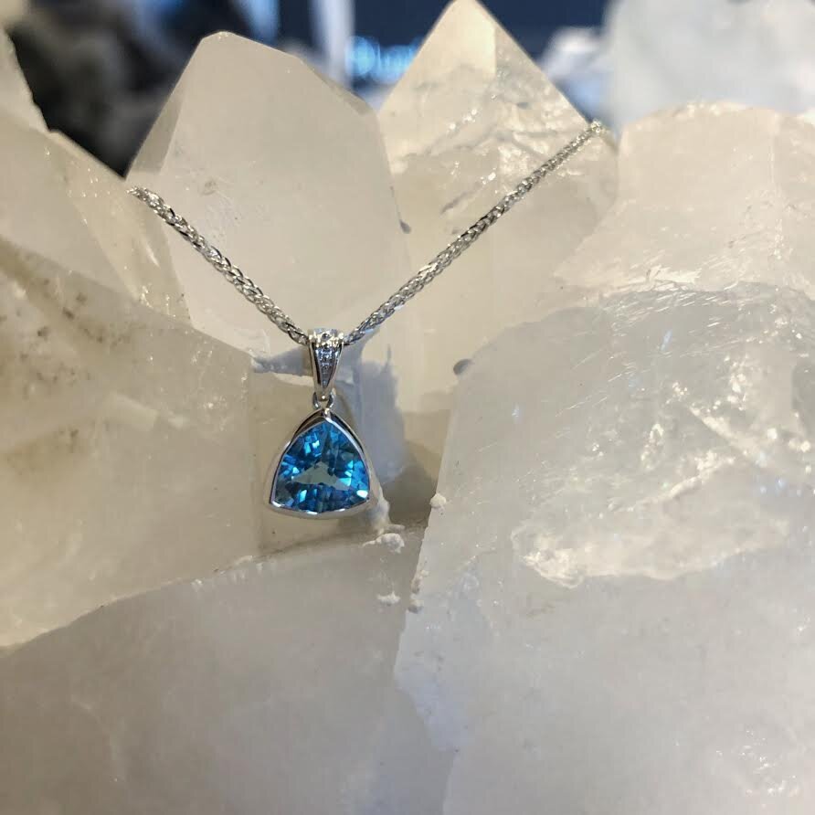 Photo of Stanton Color Trillion Blue Topaz Pendant in a decorative scene, designed by , available at Plumb Gold & Plumb Silver