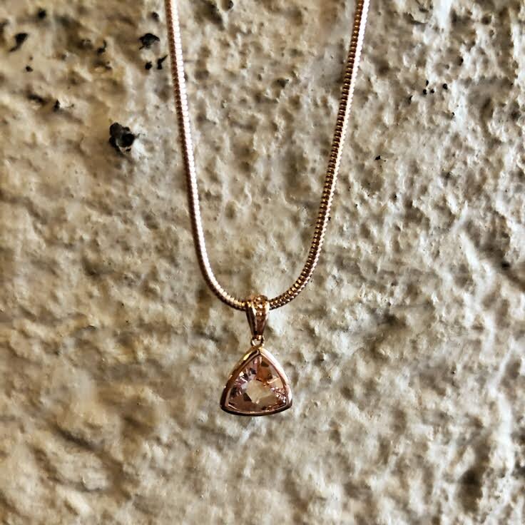 Photo of Stanton Color Trillion Morganite Bezel Pendant in a decorative scene, designed by , available at Plumb Gold & Plumb Silver