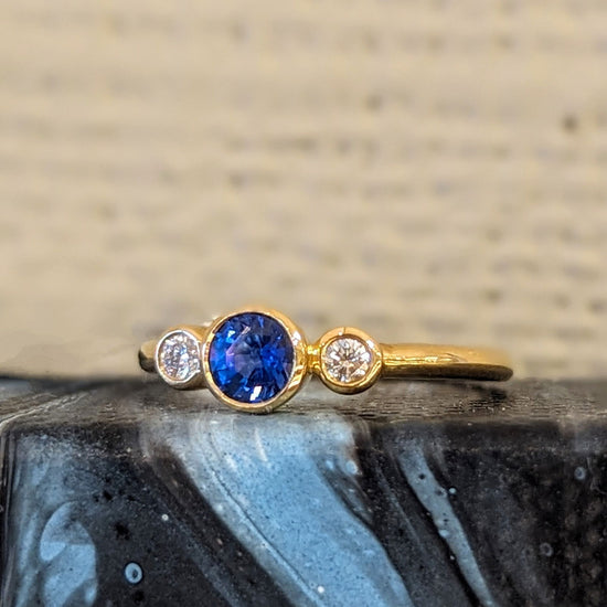 Photo of Three Stone Bezel Ring in a decorative scene, designed by , available at Plumb Gold & Plumb Silver
