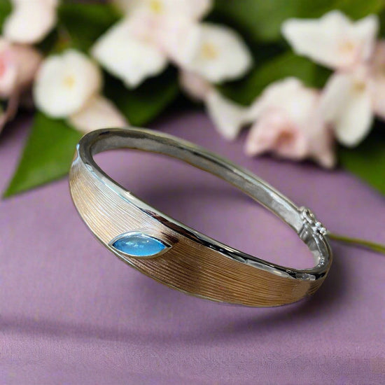 Photo of Two Tone Bangle with Blue Topaz Accent in a decorative scene, designed by , available at Plumb Gold & Plumb Silver