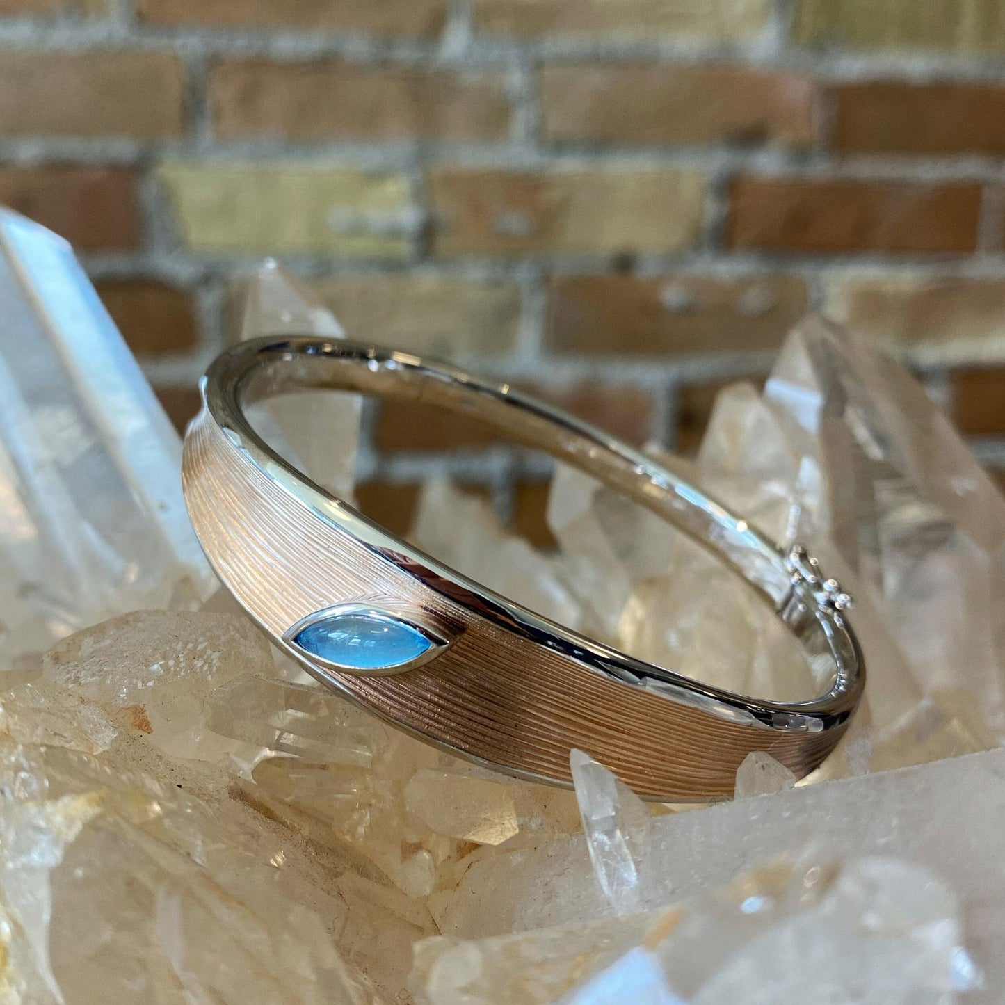 Photo of Two Tone Bangle with Blue Topaz Accent in a decorative scene, designed by , available at Plumb Gold & Plumb Silver
