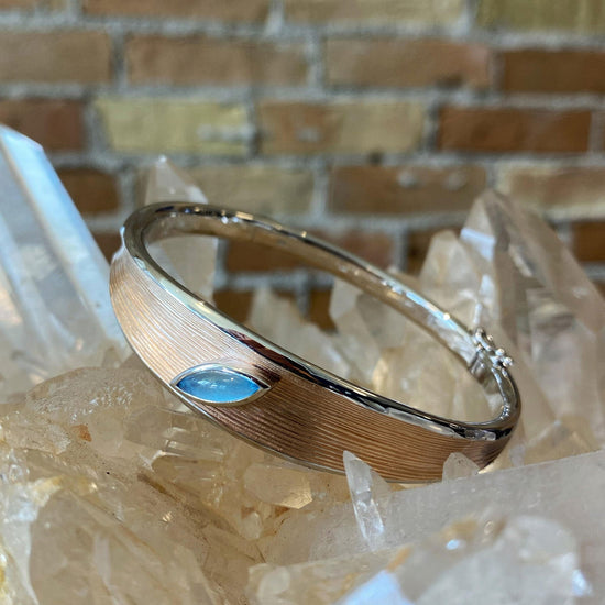 Photo of Two Tone Bangle with Blue Topaz Accent in a decorative scene, designed by , available at Plumb Gold & Plumb Silver