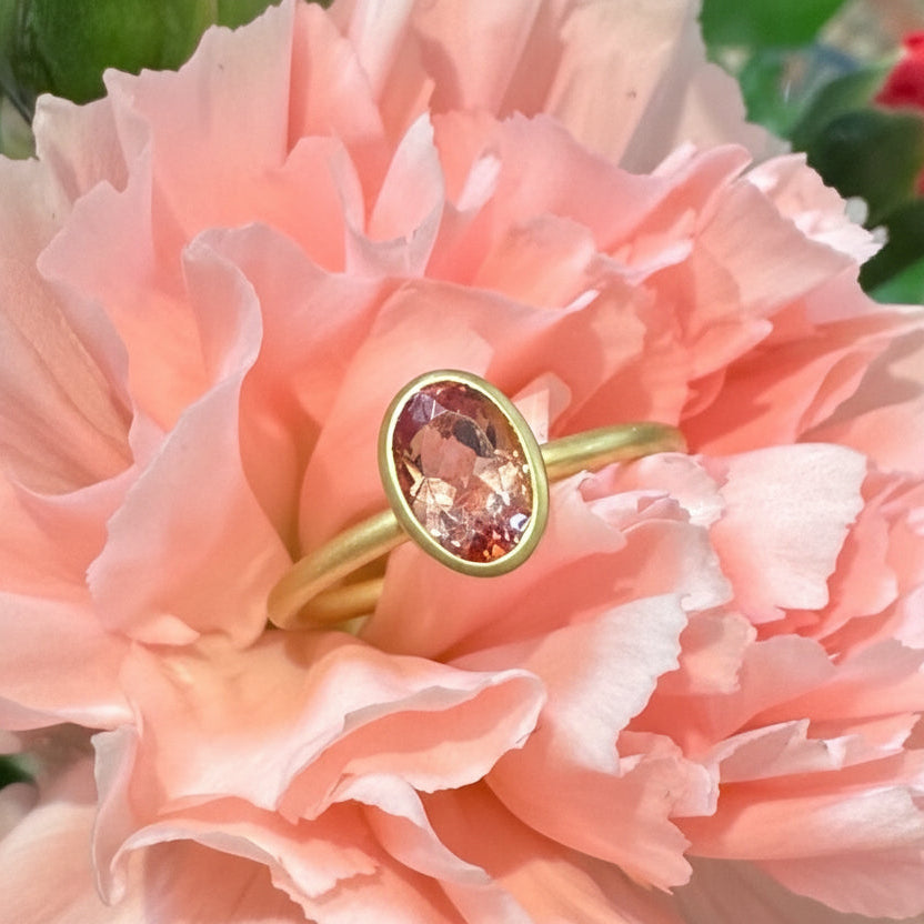 Gold ring with a pink gemstone on a pink flower